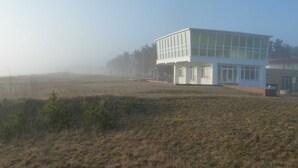 Un bâtiment moderne doté d’un toit plat et de grandes fenêtres, entouré d’un champ verdoyant et d’arbres.