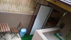 A small outdoor area with a wooden table and chairs, a blue trash bin, and a white door leading to an interior space. - Apartament w Centrum Noclegi Płock (Plock)