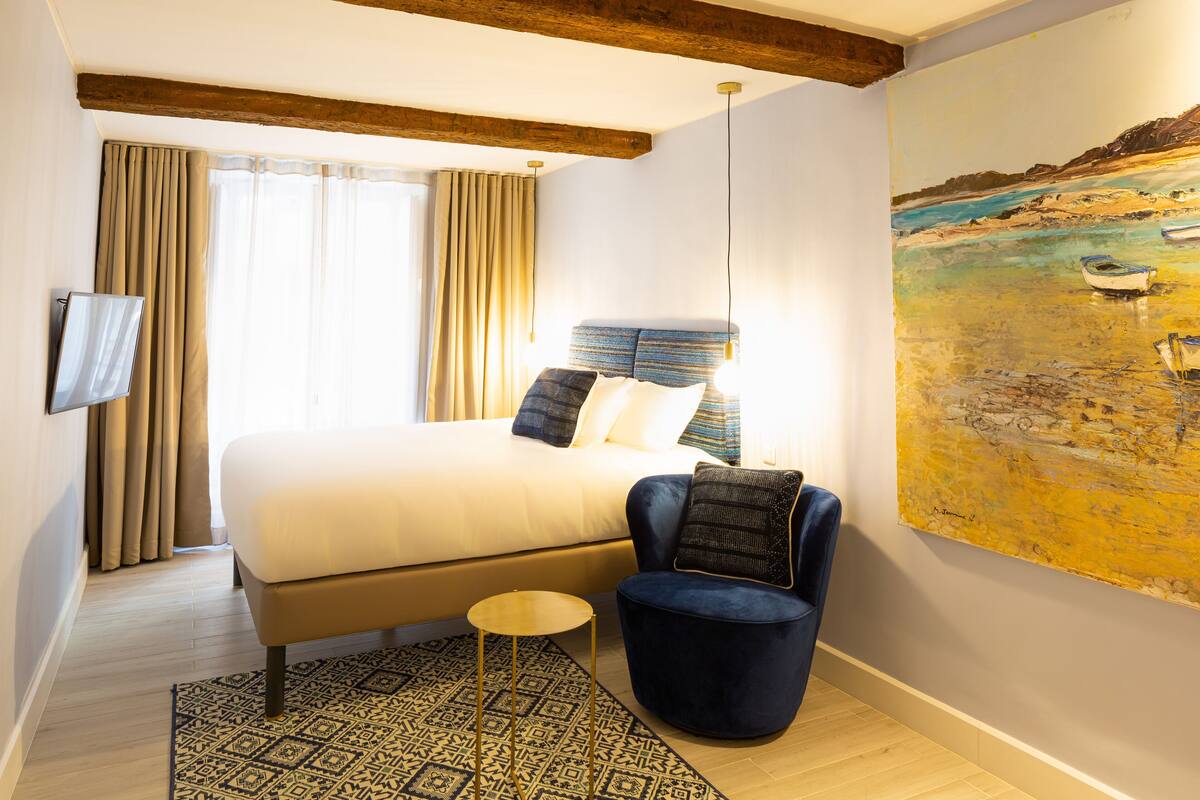 A bedroom with a bed, a chair, a painting, and a television.