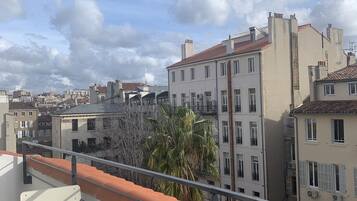 A terrace with a white table and chairs, overlooking a cityscape with buildings and a palm tree.