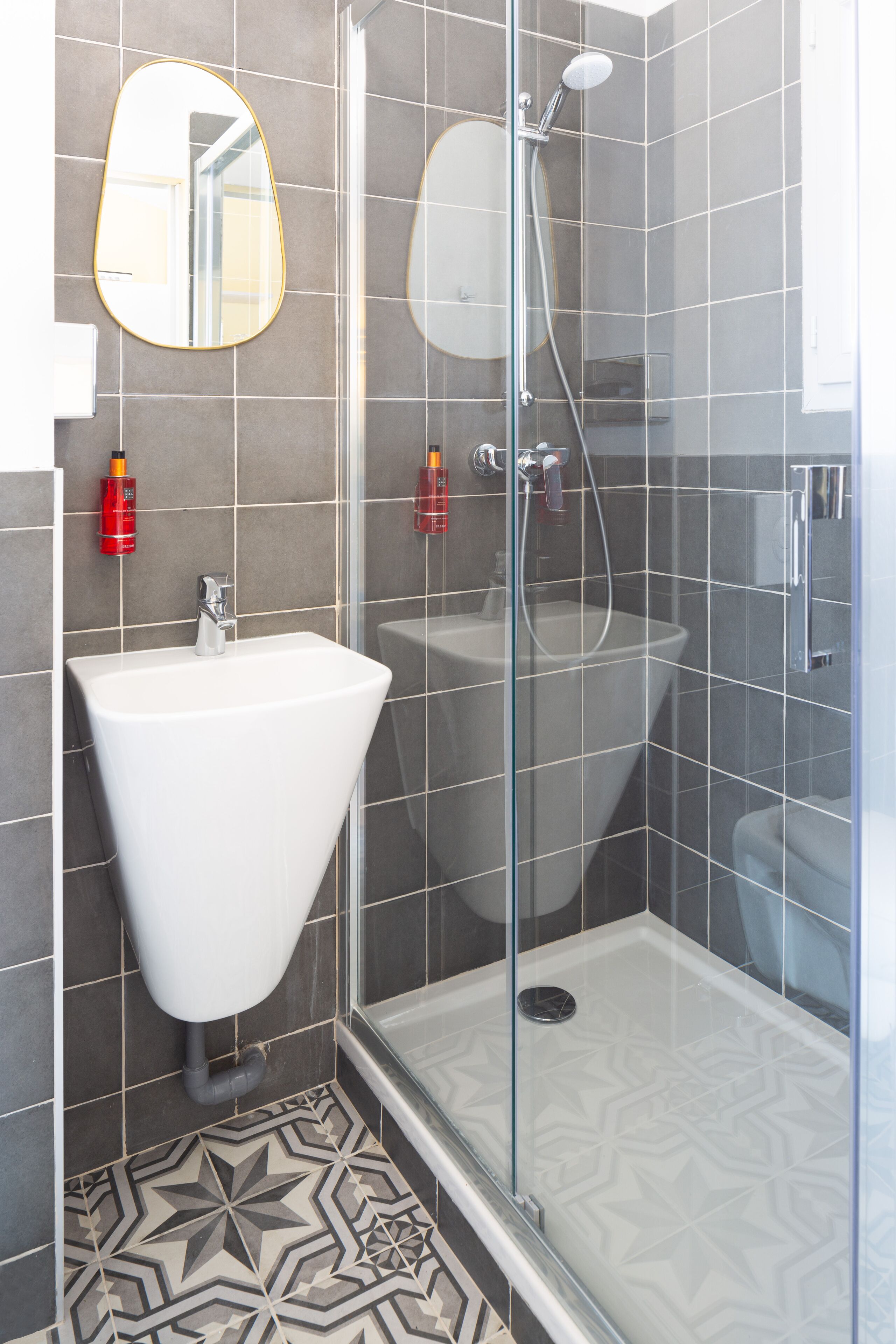 A modern bathroom with a glass-enclosed shower, a white pedestal sink, and a large mirror.