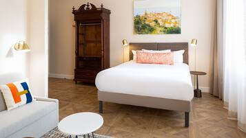 Habitación de hotel con una cama grande, un sofá, una mesita, un armario de madera y un cuadro en la pared.