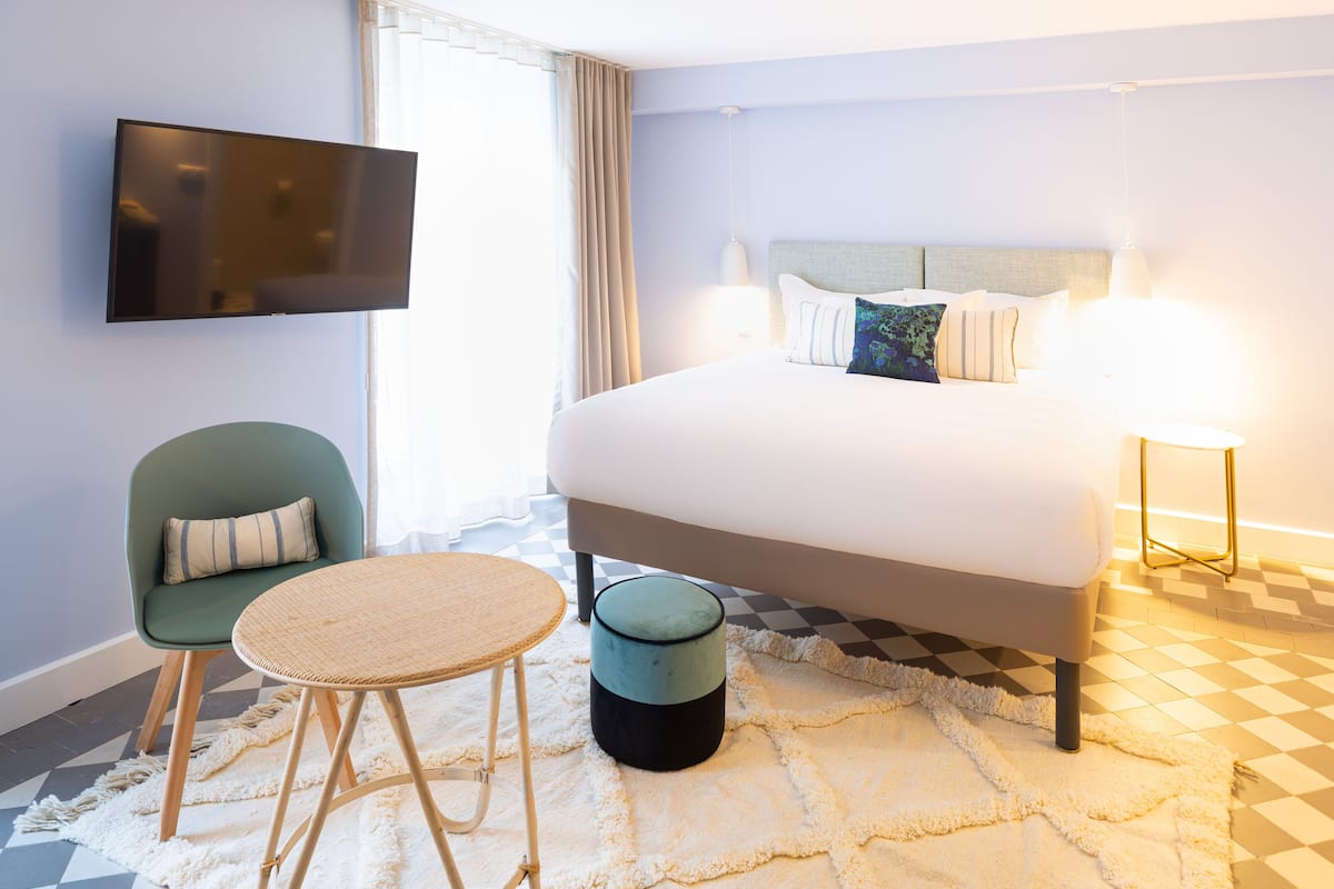 A hotel room with a bed, a television, a chair, a round table, and a lamp.