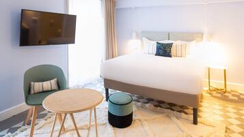 Una camera d'albergo con un letto, una televisione, una sedia, un tavolo rotondo e una lampada.