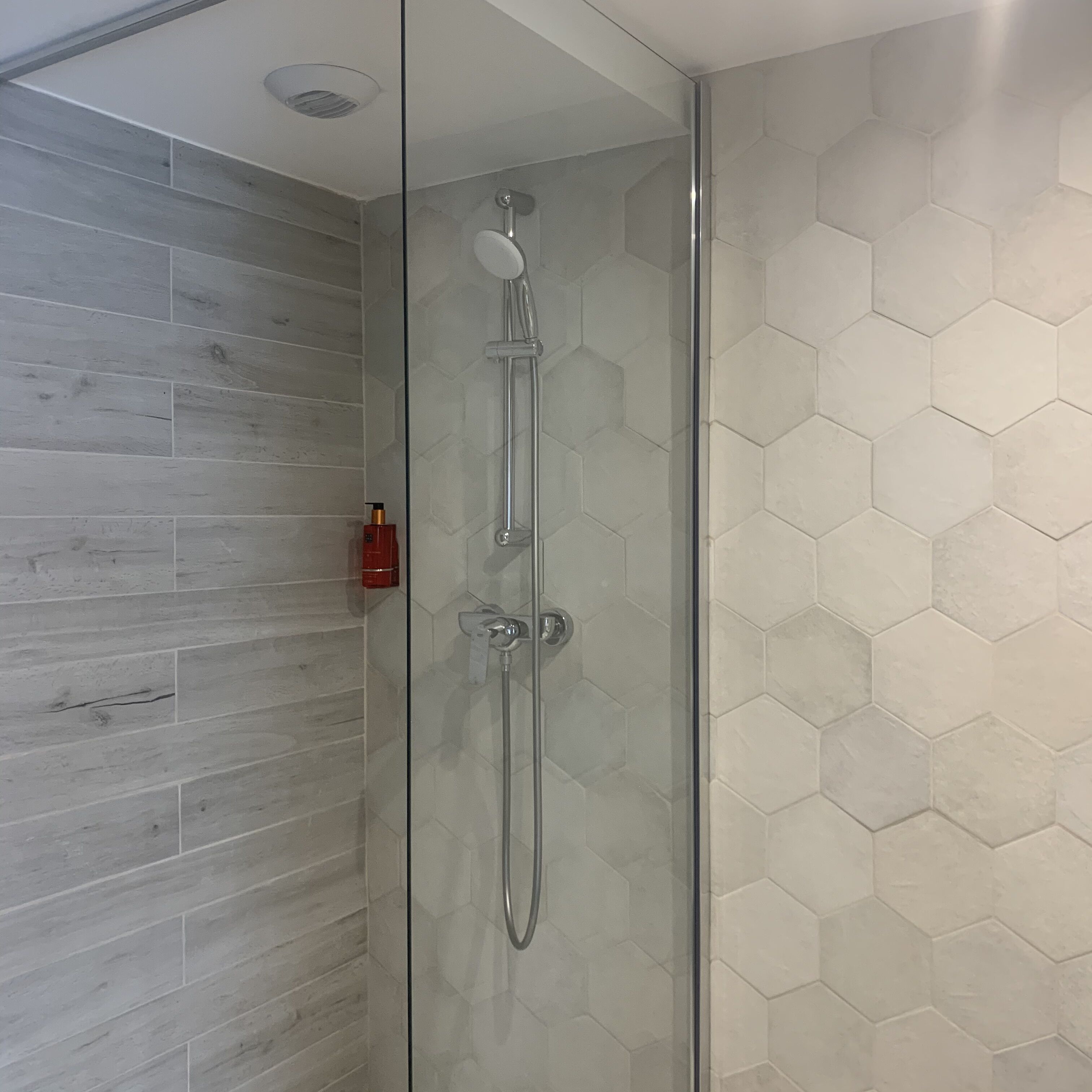 Um chuveiro envidraçado com design moderno, equipado com um chuveiro manual e painel de controle fixado na parede.