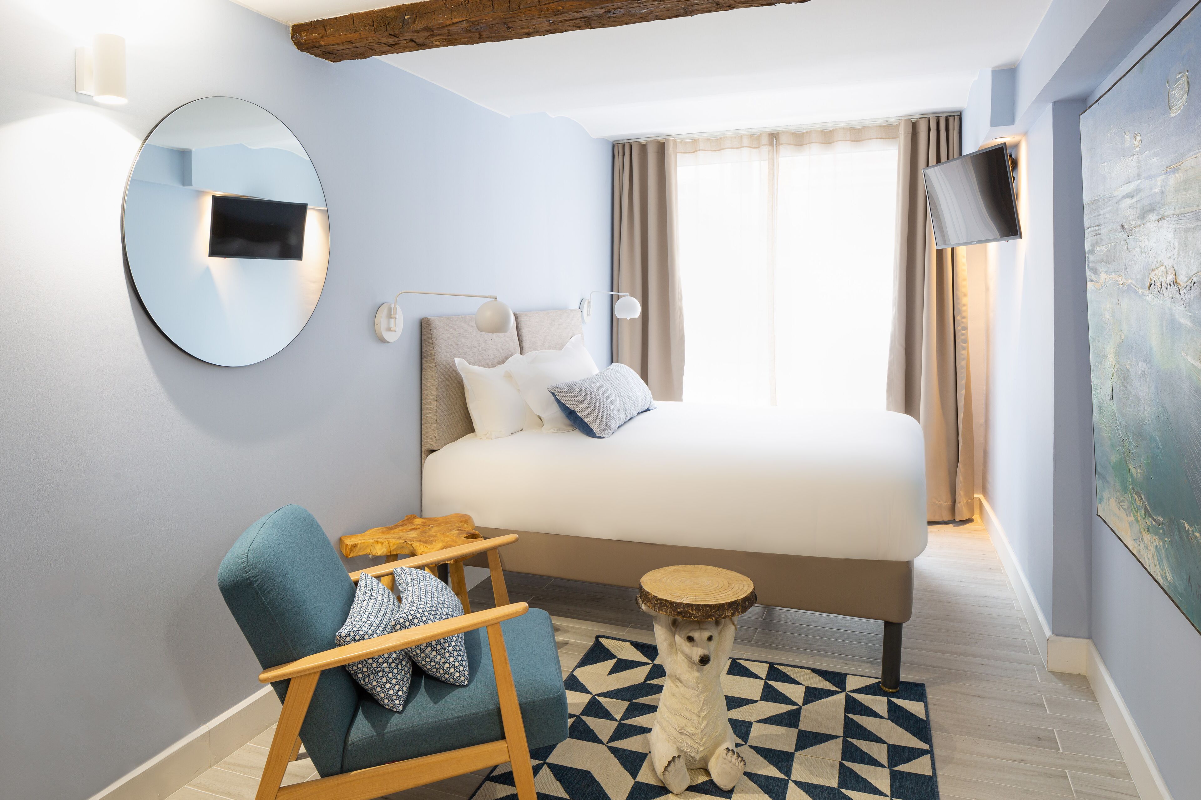 Una habitación de hotel moderna con una cama grande, un espejo redondo, una mesita pequeña y un perro de pie sobre sus patas traseras.
