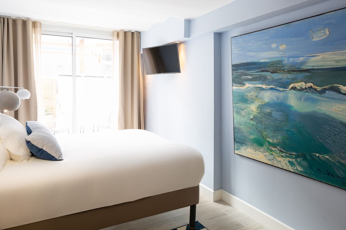 A bedroom with a large bed, a flat-screen TV mounted on the wall, and a large painting of a seascape.