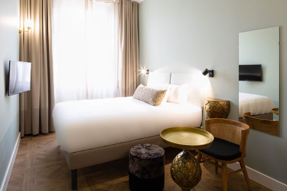 A hotel room with a large bed, a bedside table, a chair, a round table, and a wall-mounted TV.