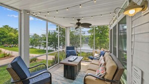 A covered outdoor seating area with a view of a lake, a ceiling fan, and string lights.