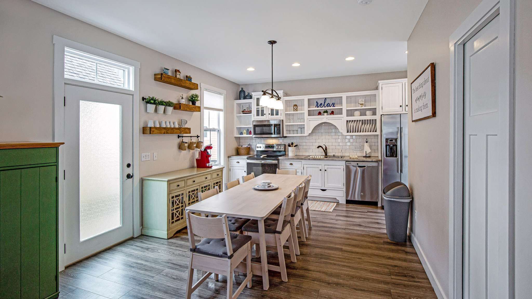 A kitchen with white cabinets, a dining table with chairs, a microwave, a stove, and a refrigerator.