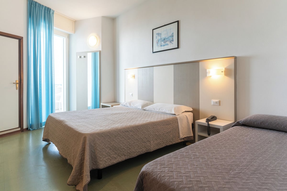 Habitación de hotel con dos camas, una mesita de noche con lámpara, teléfono y un cuadro en la pared.