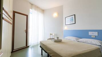 Ein Hotelzimmer mit Bett, Sessel, Wandlampe und einem fenster mit Vorhängen.