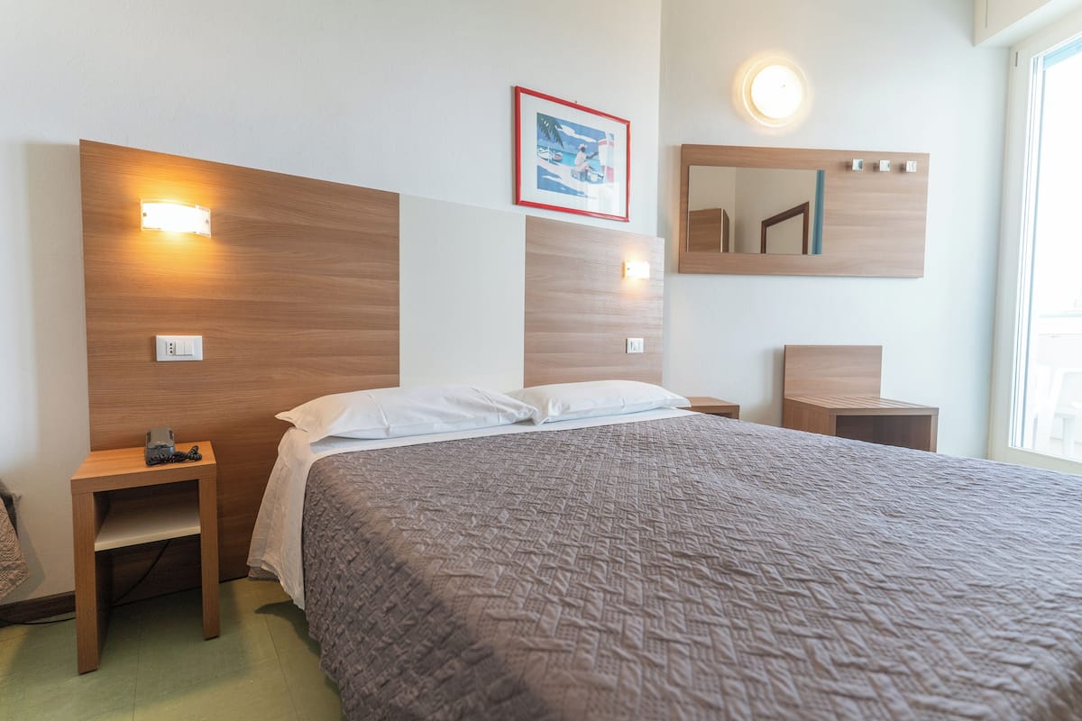 Una habitación de hotel con una cama grande, dos mesitas de noche, un espejo fijado a la pared y un cuadro enmarcado.