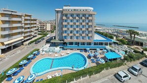 A hotel with a swimming pool, multiple balconies, and a view of the beach. - Hotel Concord (Ravenna)