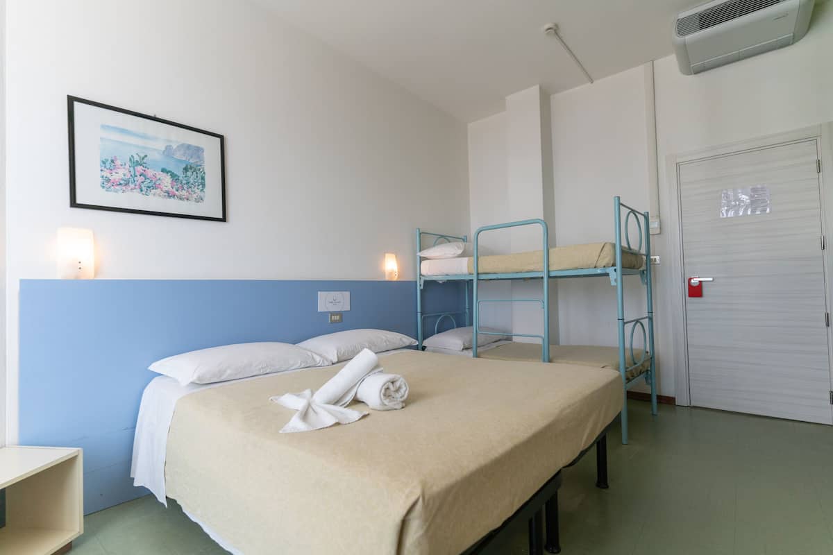 Una cama individual con una manta color beige, un cabecero azul y un aire acondicionado instalado en la pared.