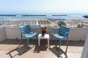 A balcony with two chairs and a table, overlooking a beach with rows of sunbeds. - Hotel Concord (Ravenna)