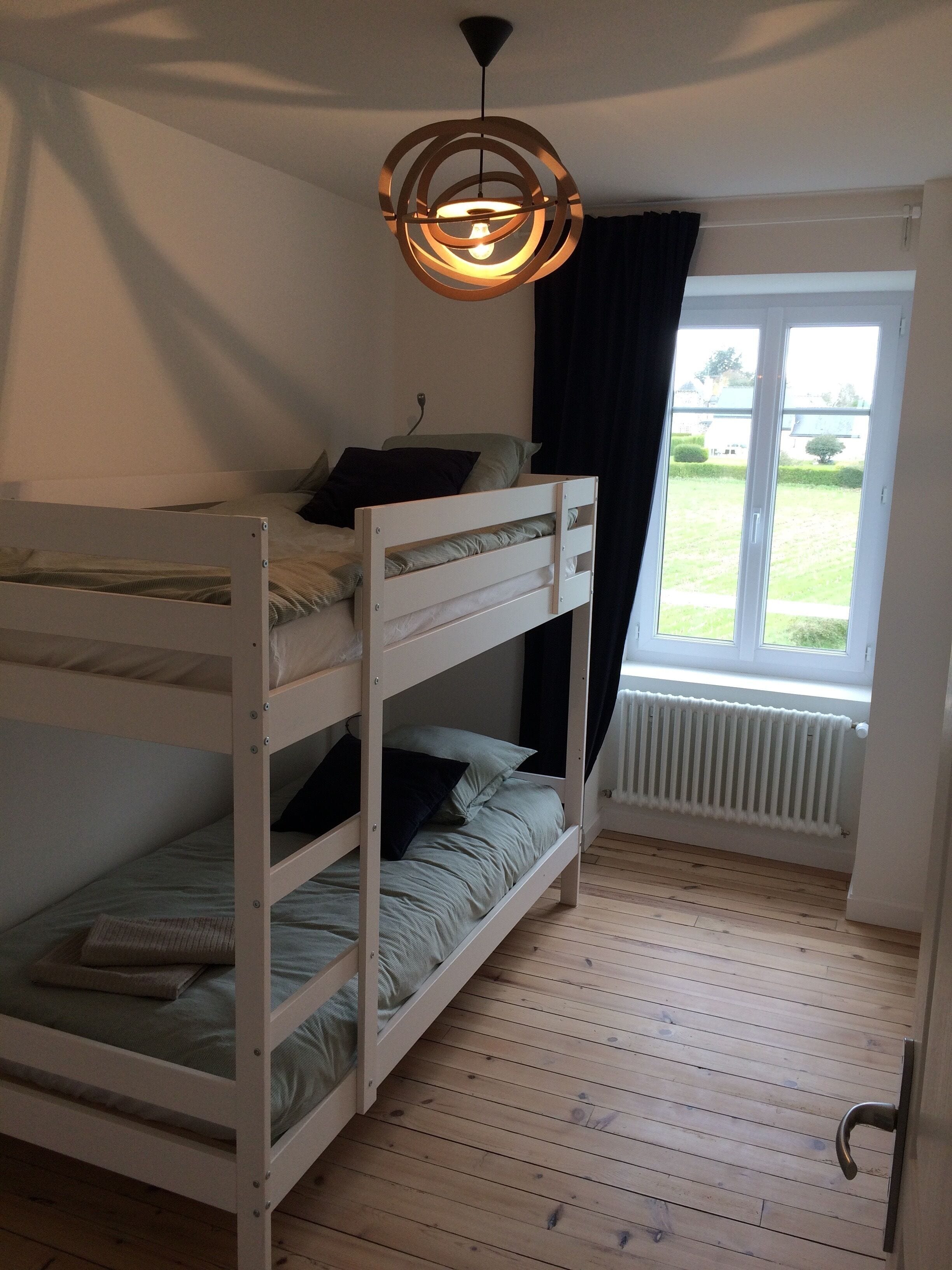 A bunk bed room with a window, a radiator, and a hanging light fixture.