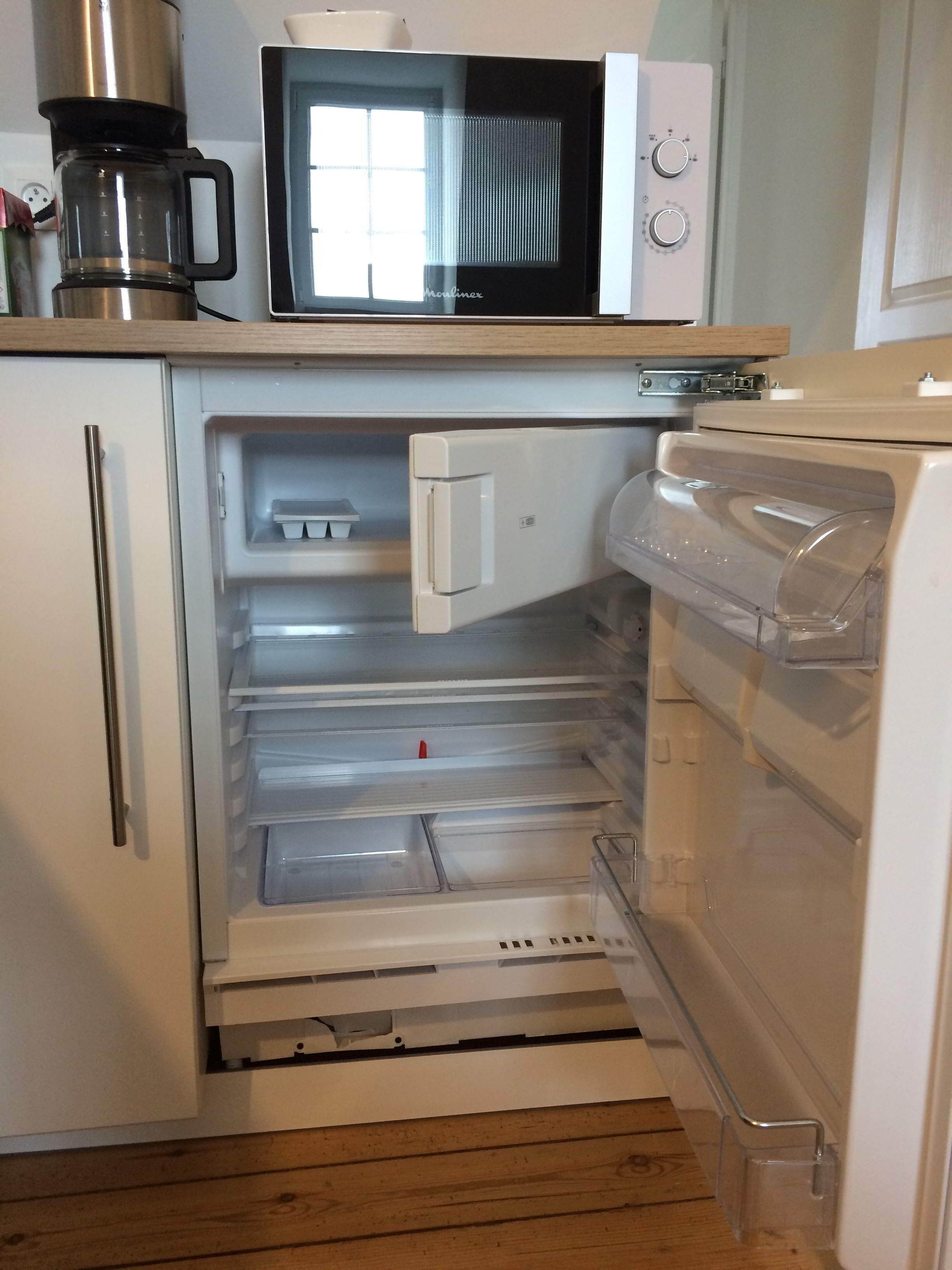 A compact kitchen with a microwave, coffee maker, and a refrigerator with a freezer drawer.