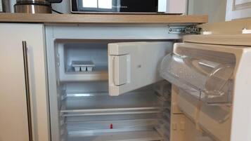 A compact kitchen with a microwave, coffee maker, and a refrigerator with a freezer drawer.
