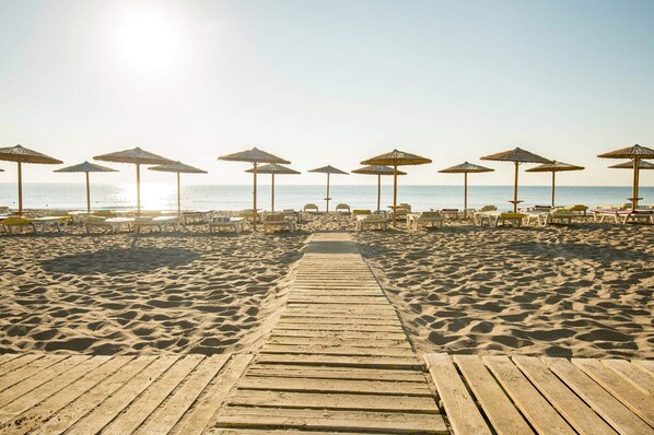 A wooden boardwalk leading to beach umbrellas and lounge chairs.