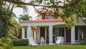 Ein modernes Haus mit überdachter Veranda, zwei weißen Lounge-Stühlen und einem gepflegten Rasen.