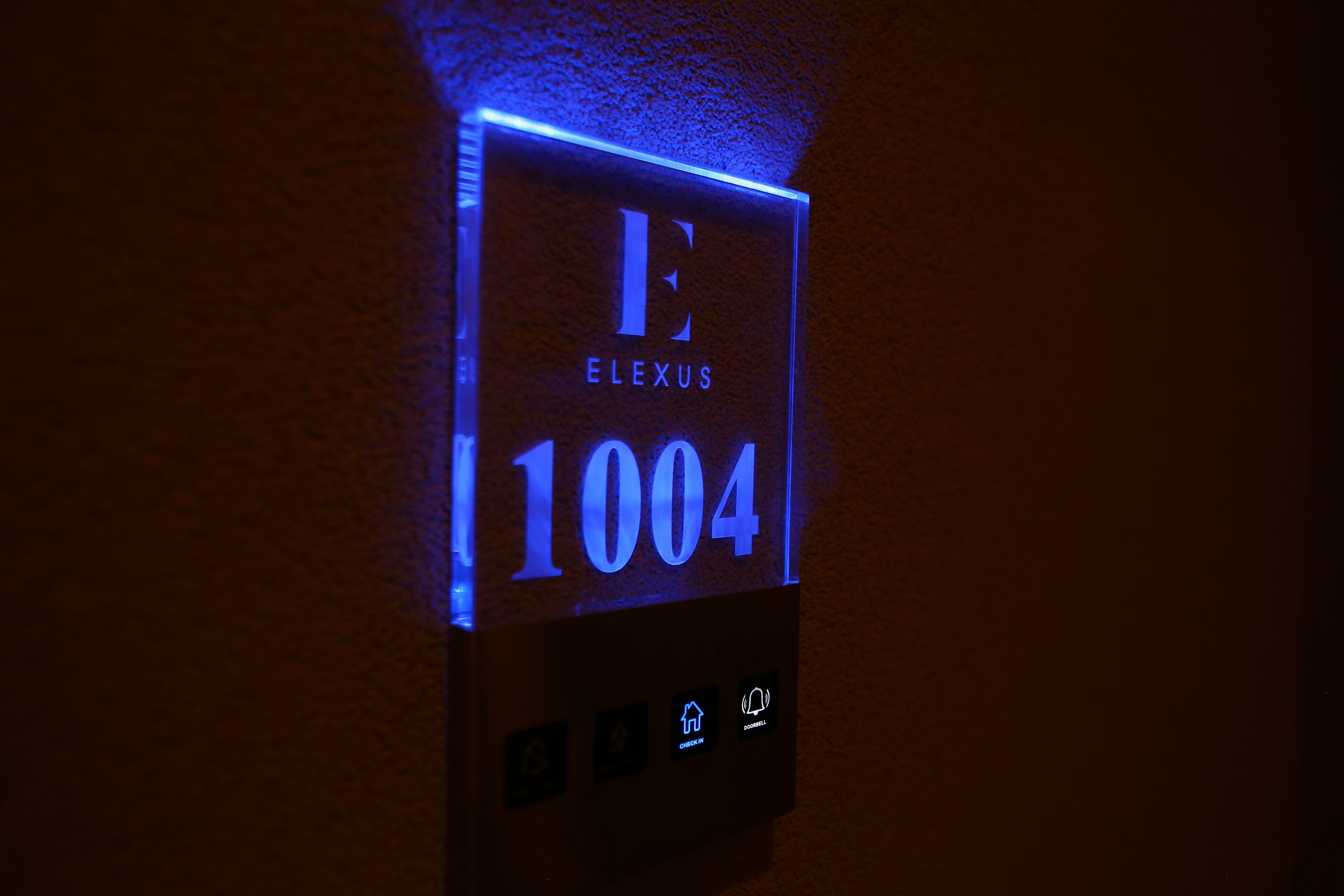 A digital elevator control panel with illuminated floor number 1004 and the name "ELEXUS".