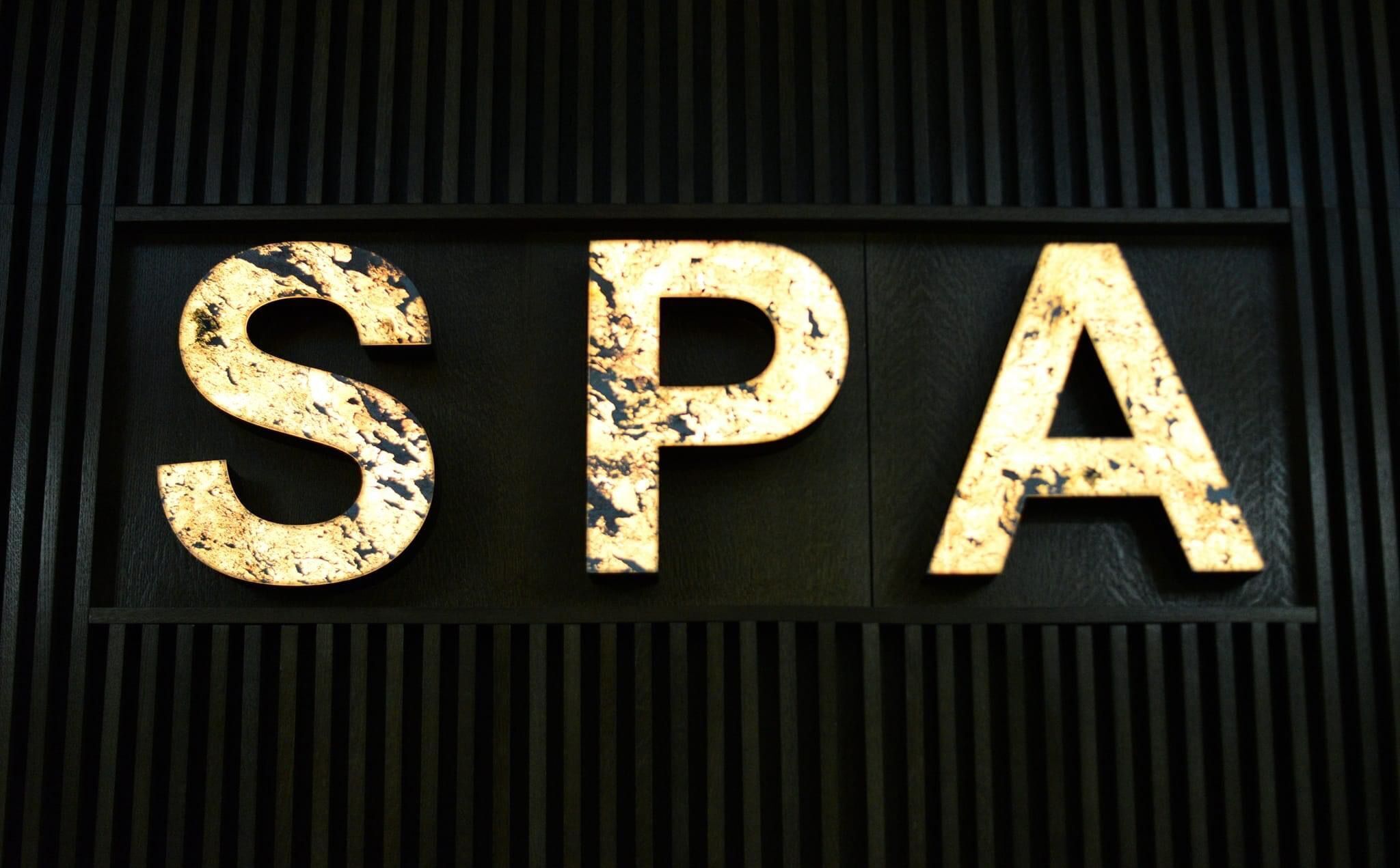 A sign with the letters "SPA" in a distressed, gold-colored font against a dark background with vertical lines.