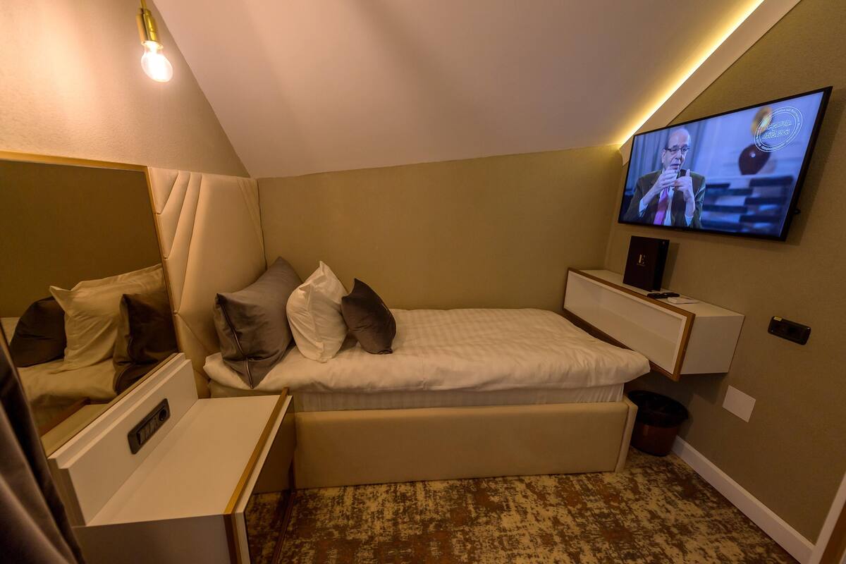 A hotel room with a bed, a television mounted on the wall, and a small desk with a lamp.
