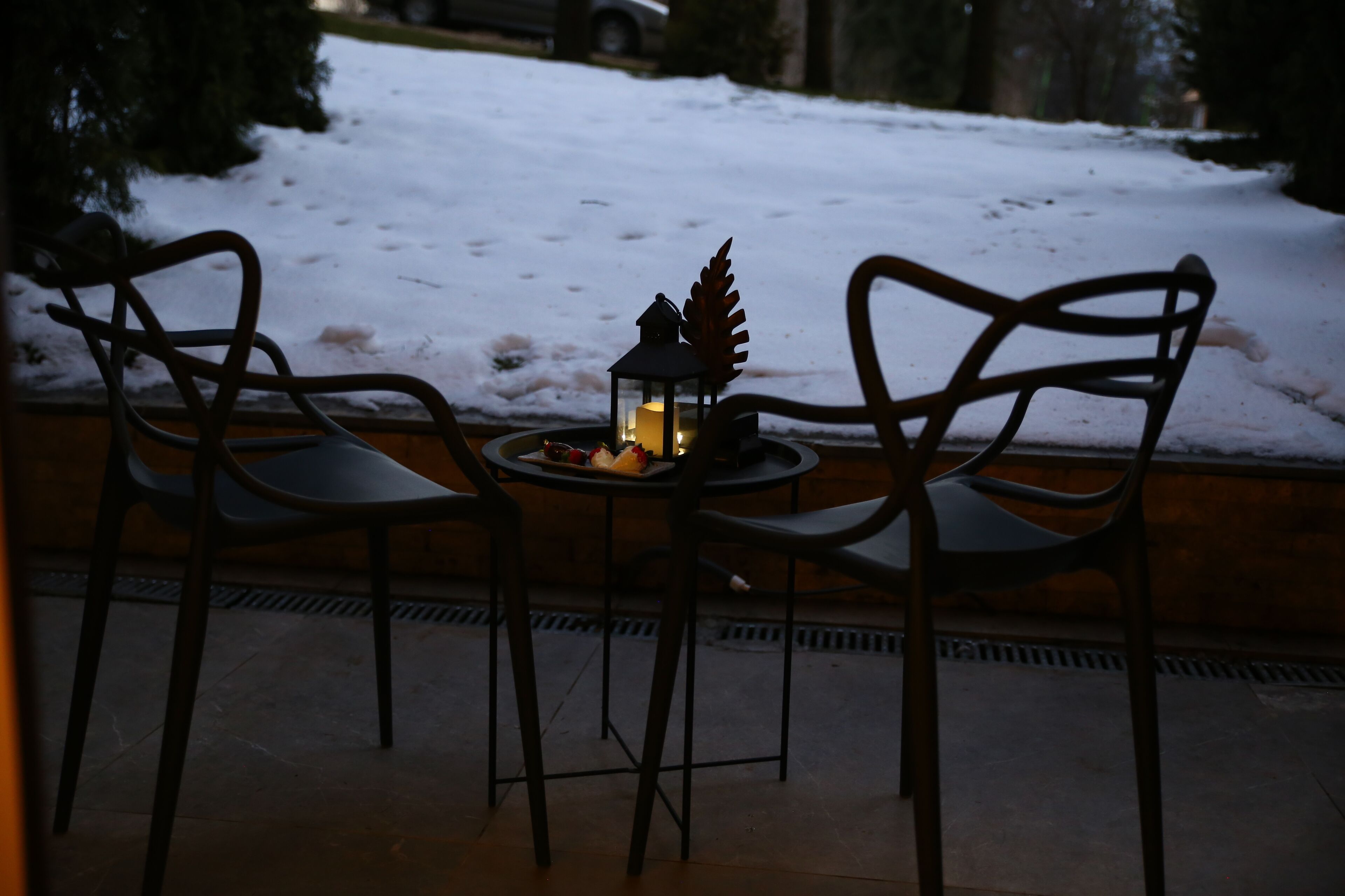 Una mesa con dos sillas, un farol y un adorno en un patio nevado.