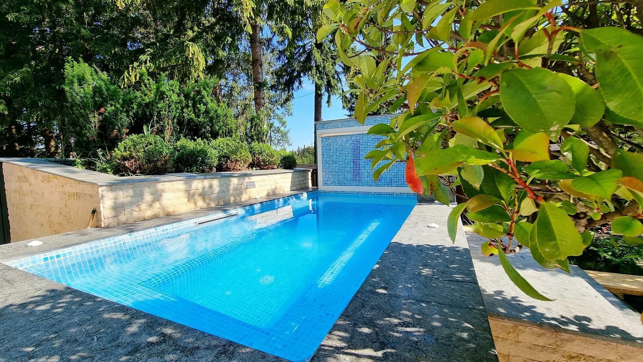 Una piscina rectangular con agua azul cristalina, rodeada por un solárium de concreto y un bajo muro de piedra.