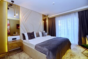 A modern hotel room with a large bed, a bedside table, a mirror, and a view of the outdoors through sheer curtains.
