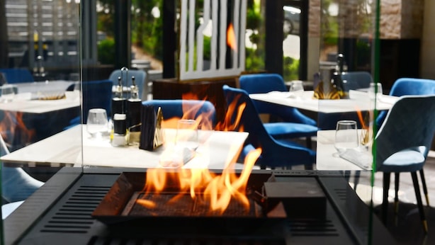 An outdoor dining area with tables, chairs, and a central fire feature. - Elexus (Predeal)