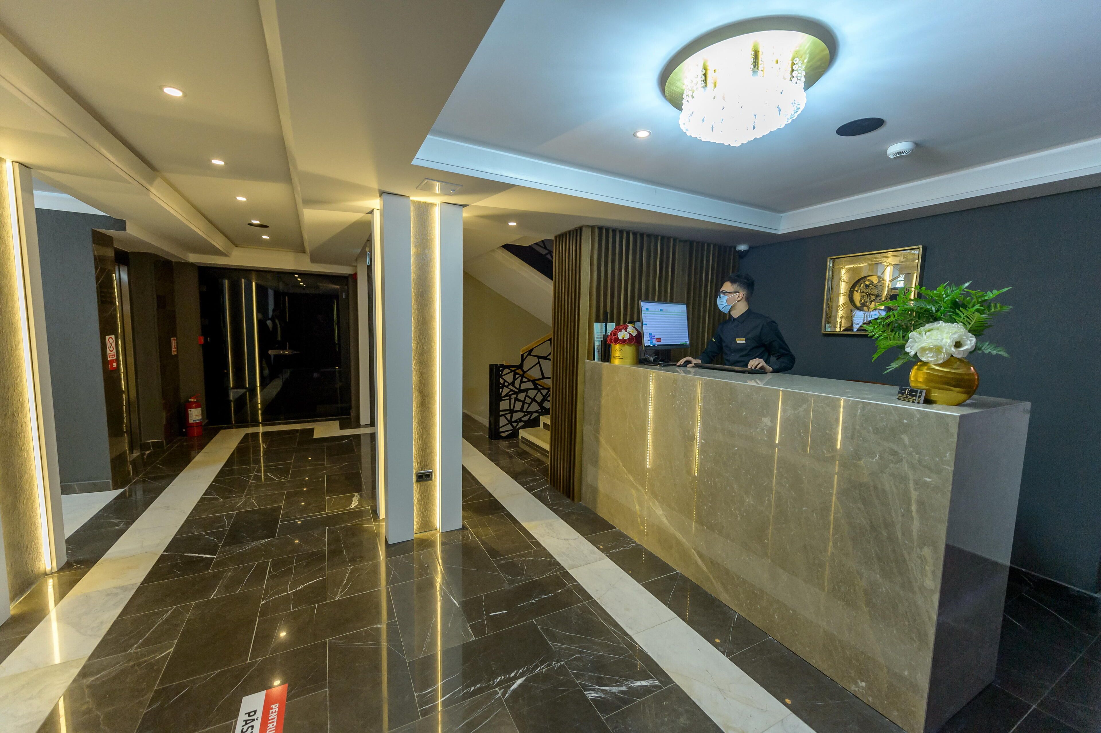 A hotel reception area with a marble floor, a reception desk, a computer monitor, and a decorative plant.