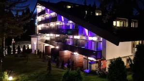 A modern multi-story building with a sloped roof, illuminated by purple lighting. - Elexus (Predeal)