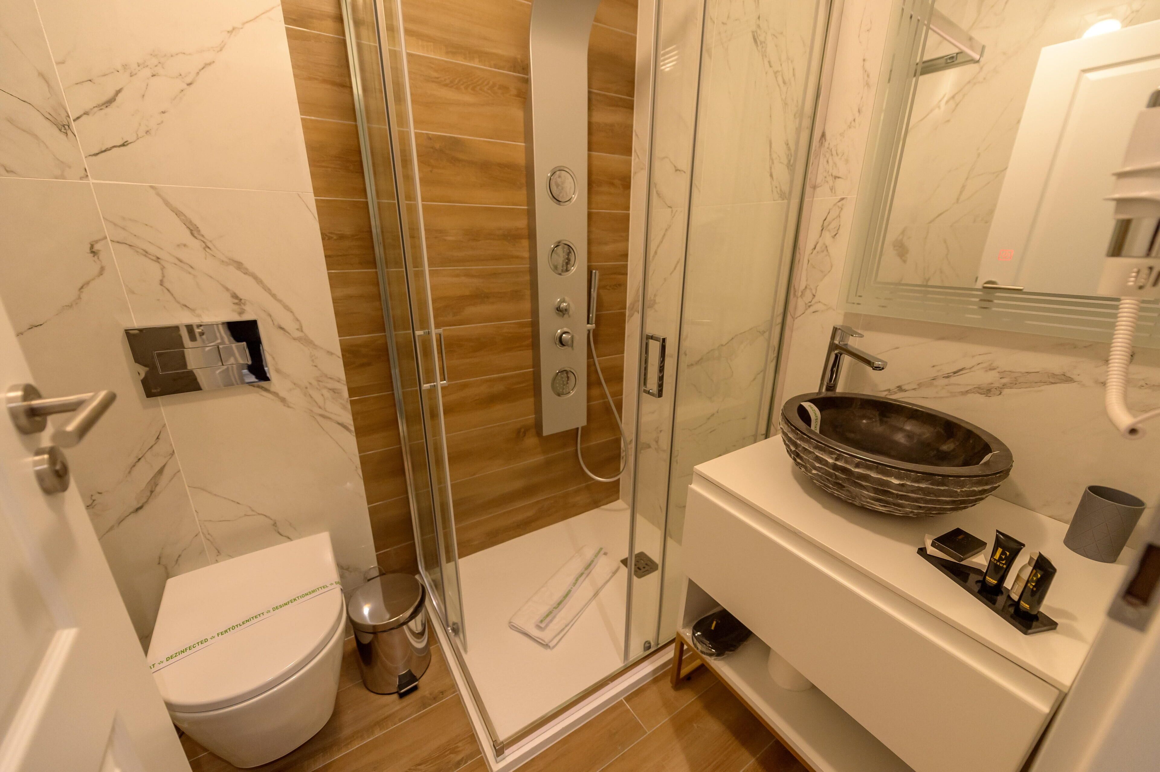 A modern bathroom with a glass-enclosed shower, a white toilet, and a marble-tiled vanity with a sink.