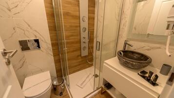 A modern bathroom with a glass-enclosed shower, a white toilet, and a marble-tiled vanity with a sink.