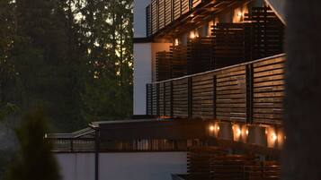 A multi-story building with balconies and outdoor lighting, surrounded by trees.