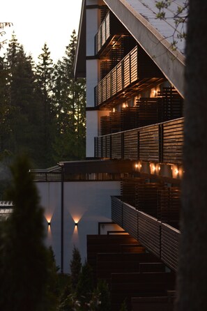 A multi-story building with balconies and outdoor lighting, surrounded by trees.