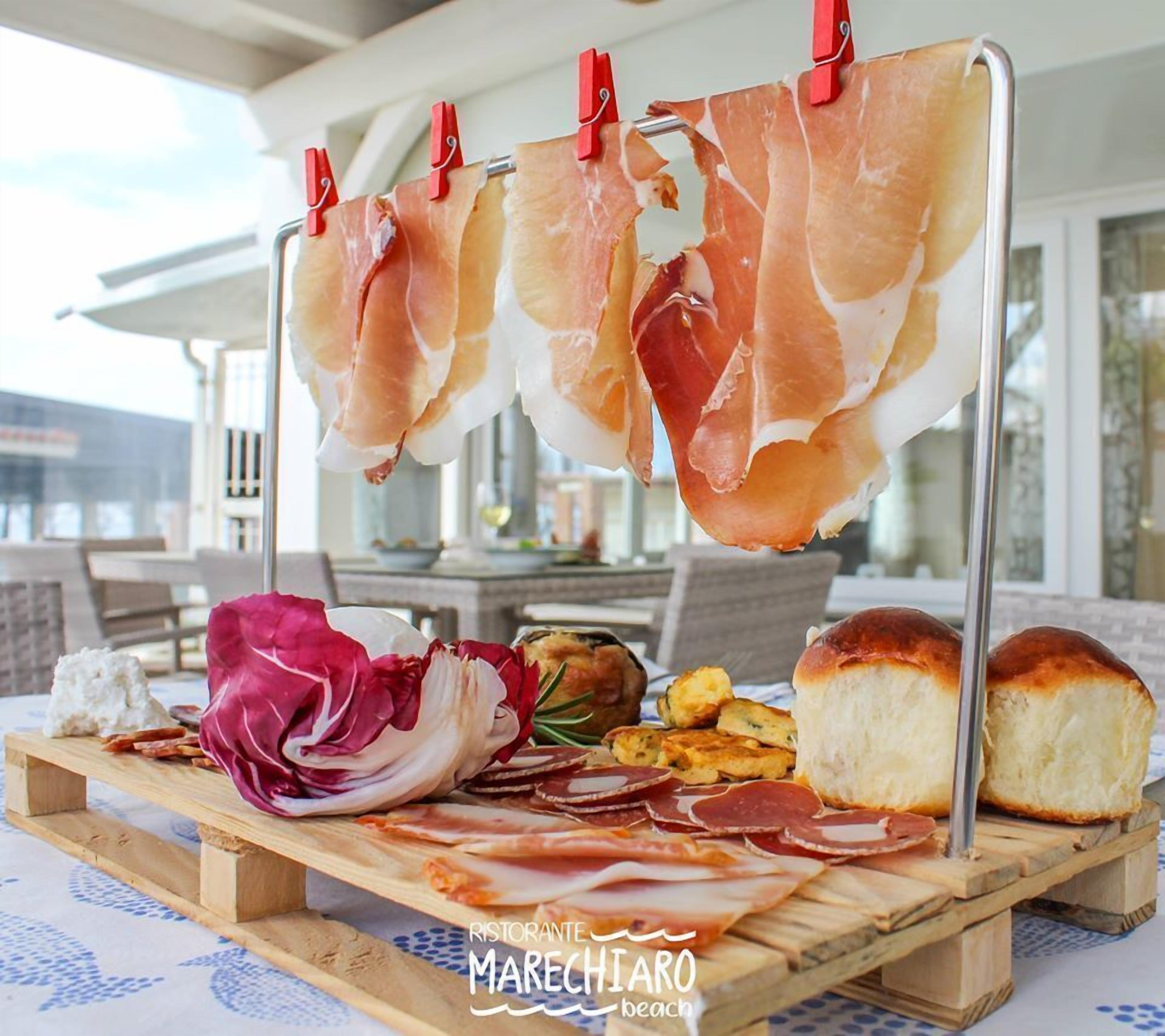 Una tabla de madera con diversos alimentos, como jamón serrano, queso y pan, expuesta al aire libre.