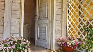 A wooden building entrance with a stone staircase leading up to a door. There are two flower pots with pink and white flowers on either side of the door. - Marechiaro Paestum (Capaccio-Paestum)