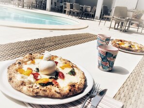 A dining table with a pizza and a drink, near a poolside area with chairs and tables. - Marechiaro Paestum (Capaccio-Paestum)