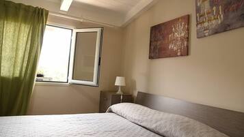 A bedroom with a bed, a nightstand with a lamp, a window with curtains, and two wall art pieces.