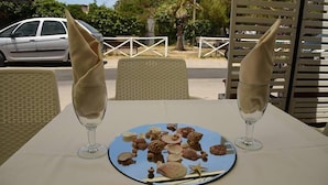 A table with a blue plate of seashells and starfish, two wine glasses with folded napkins, wicker chairs, and a white fence in the background. - Marechiaro Paestum (Capaccio-Paestum)