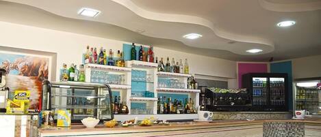 A bar area with shelves of bottles, a tiled floor, and a counter with food items.