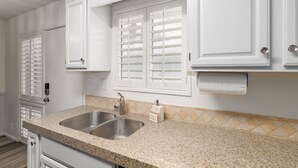 A kitchen with white cabinets, a granite countertop, a double sink, and a window with shutters. - Walk to Fashion Square Mall | Cozy Condo (Scottsdale)