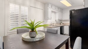A modern kitchen with white cabinets, a black refrigerator, and a dining table with a plant centerpiece. - Walk to Fashion Square Mall | Cozy Condo (Scottsdale)