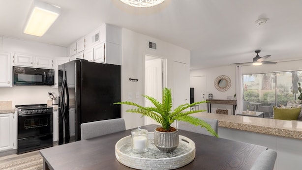 A modern kitchen with white cabinets, a black refrigerator, and a dining area with a dark wooden table. - Walk to Fashion Square Mall | Cozy Condo (Scottsdale)