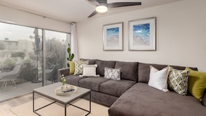 A modern living room with a grey sectional sofa, a coffee table, and two framed artworks on the wall. - Walk to Fashion Square Mall | Cozy Condo (Scottsdale)