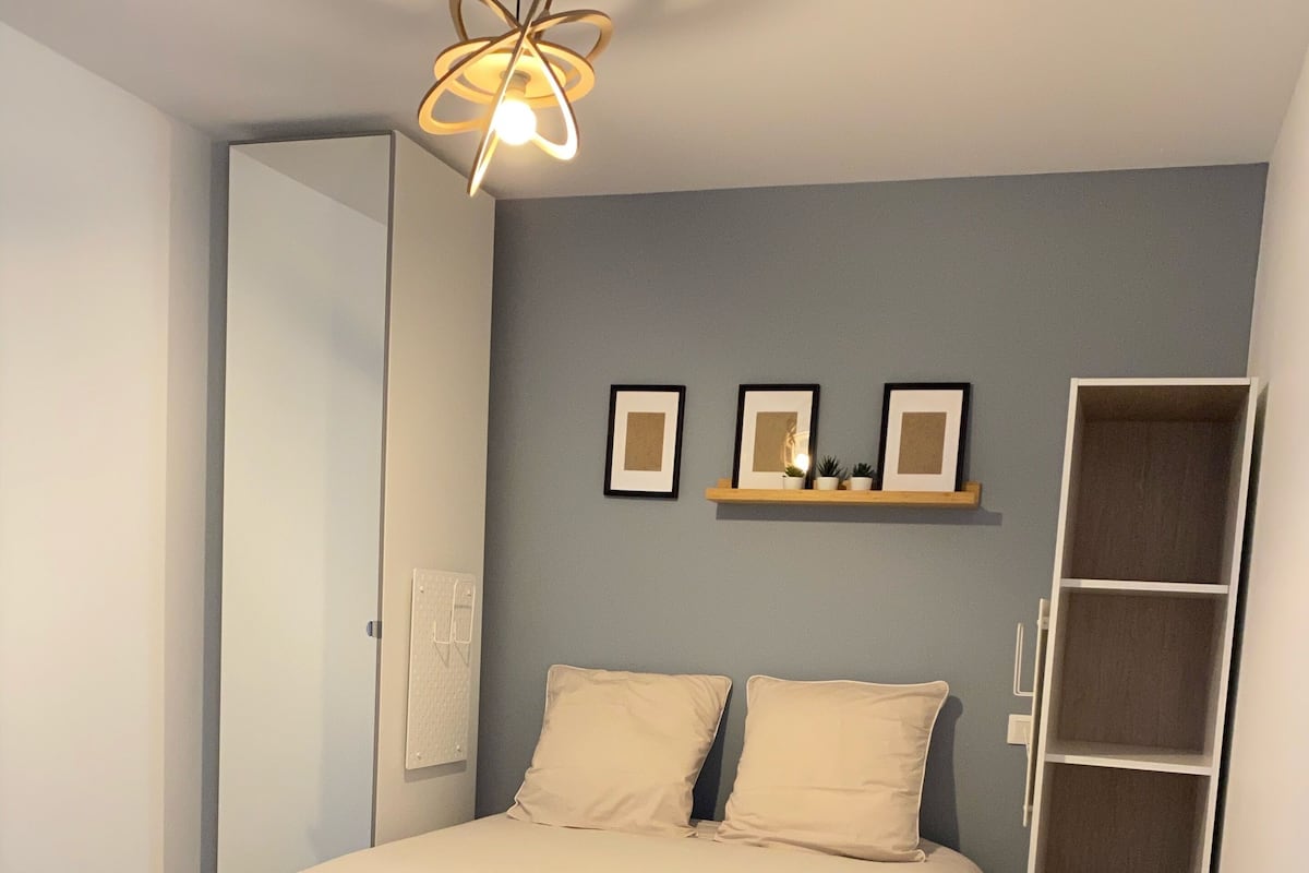 Ein Schlafzimmer mit einem Bett, einem Nachttisch, einem Kleiderschrank und einer Pendelleuchte.