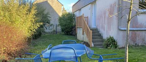 A backyard with a table and chairs, a wooden staircase, and a building with a chimney.